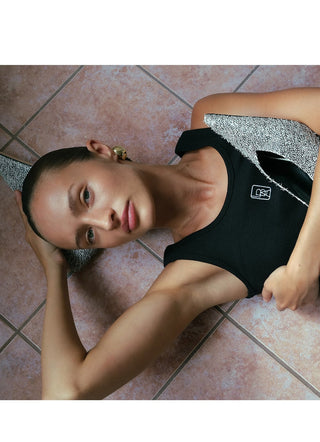 Person lying on a tiled floor wearing a black outfit with a logo.
