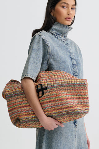Woman holding a multicolored woven bag with a plain background